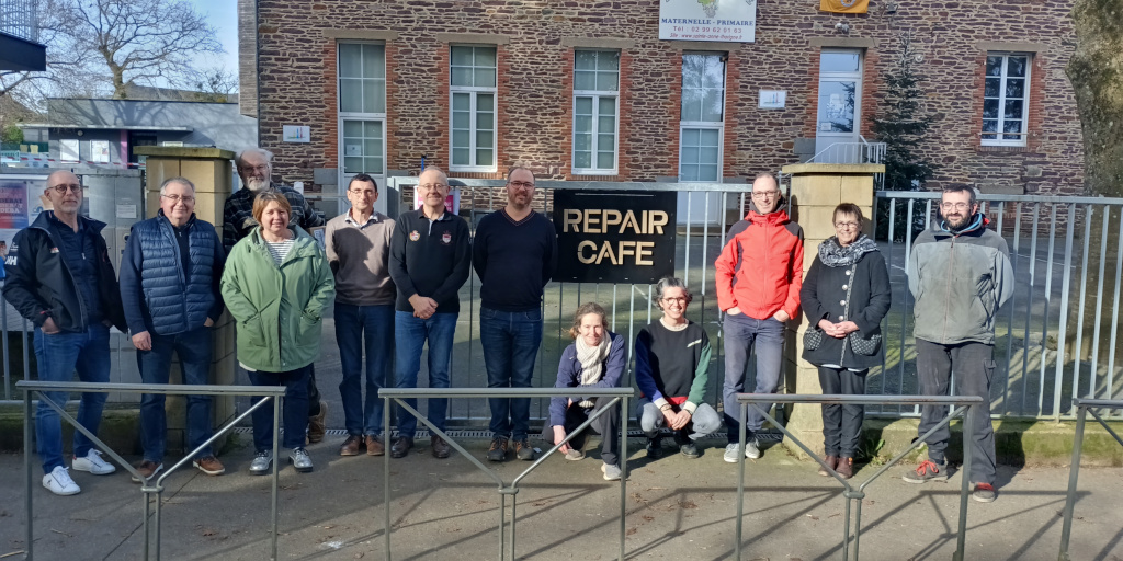 photo de nos bénévoles souriant devant l'école sainte anne, entourant un panneau Repair Café